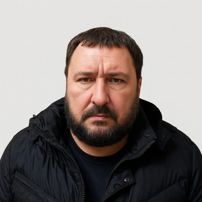 Силует на мъж с рунтава брада и сериозен поглед в тъмен пухкав яке.