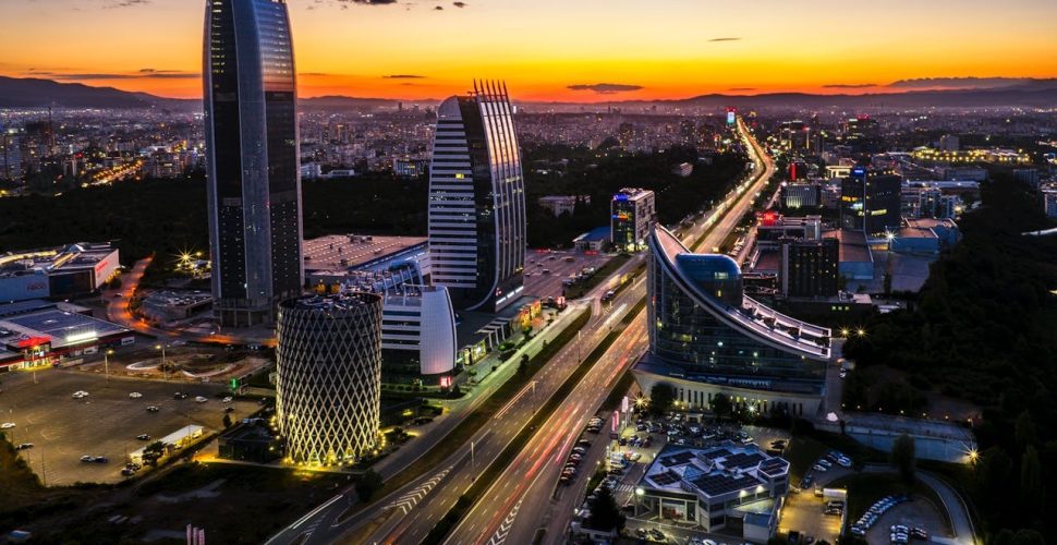 Модерен Градски Пейзаж при Залез Модерен градски пейзаж при залез с високи сгради и оживена атмосфера.