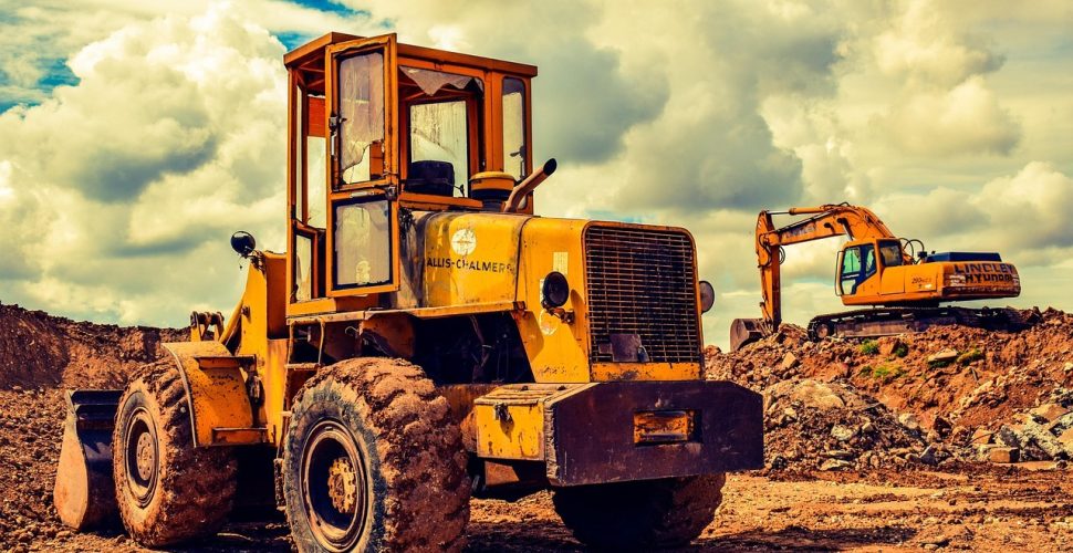 Жълт строителен трактор и екскаватор на строителен обект с небе от облаци.