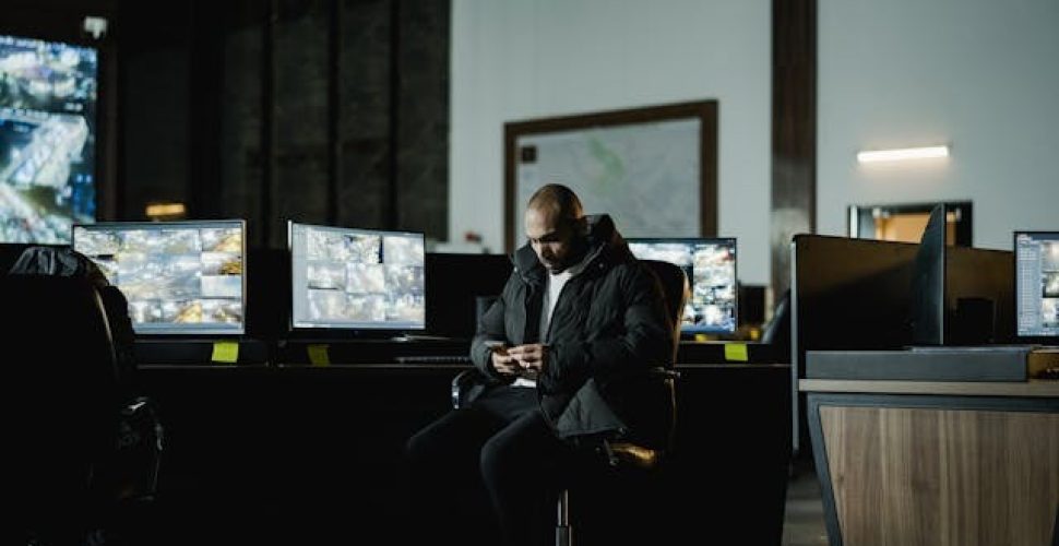 Мъж в контролна стая с мониторинг на камери Мъж в контролна стая с мониторинг на камери и смартфон в ръка.