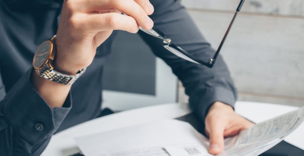 Мъж Преглежда Документи С Очила в Офис Мъж в офис преглежда документи с очила, демонстрирайки професионален фокус и анализ.