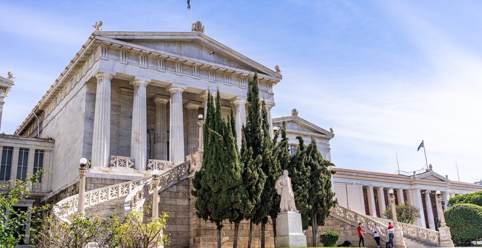 Великолепна неокласическа сграда в Атина с колонни, статуя и зеленина.