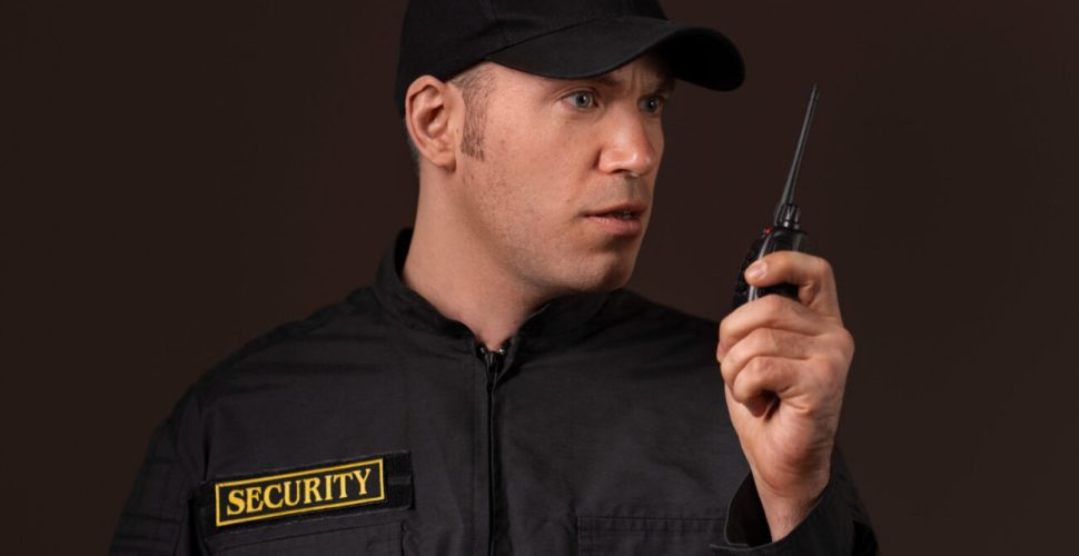 Охранител В Готовност За Действие Сериозен охранител комуникира по радиостанция, изразявайки професионализъм и готовност за действия.