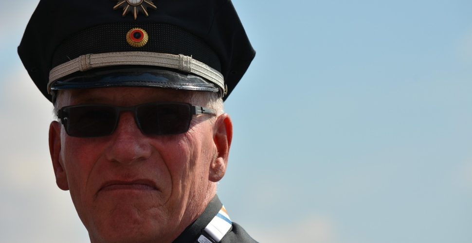 Старши ветеран в униформа с военна шапка и медали на фона на небето.